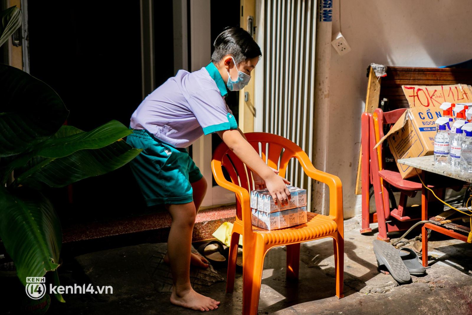 Một em nhỏ nhận quà sữa TH true MILK do đại diện Hội Phụ nữ phường Nguyễn Cư Trinh, Quận 1 gửi tới, phần quà đặt trên chiếc ghế ở trước cửa, để đảm bảo  giãn cách xã hội.